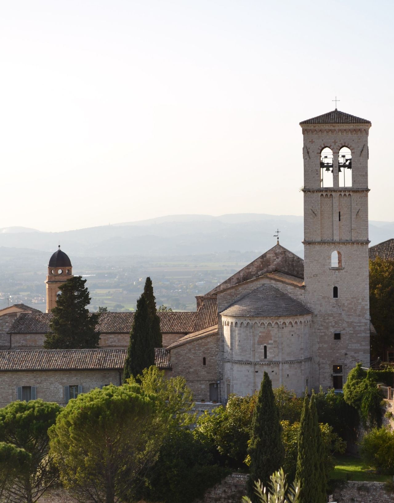 Pink and white stone church facade of the Basilica di Santa Chiara with bell tower against blue sky, Assisi, Umbria, Italy