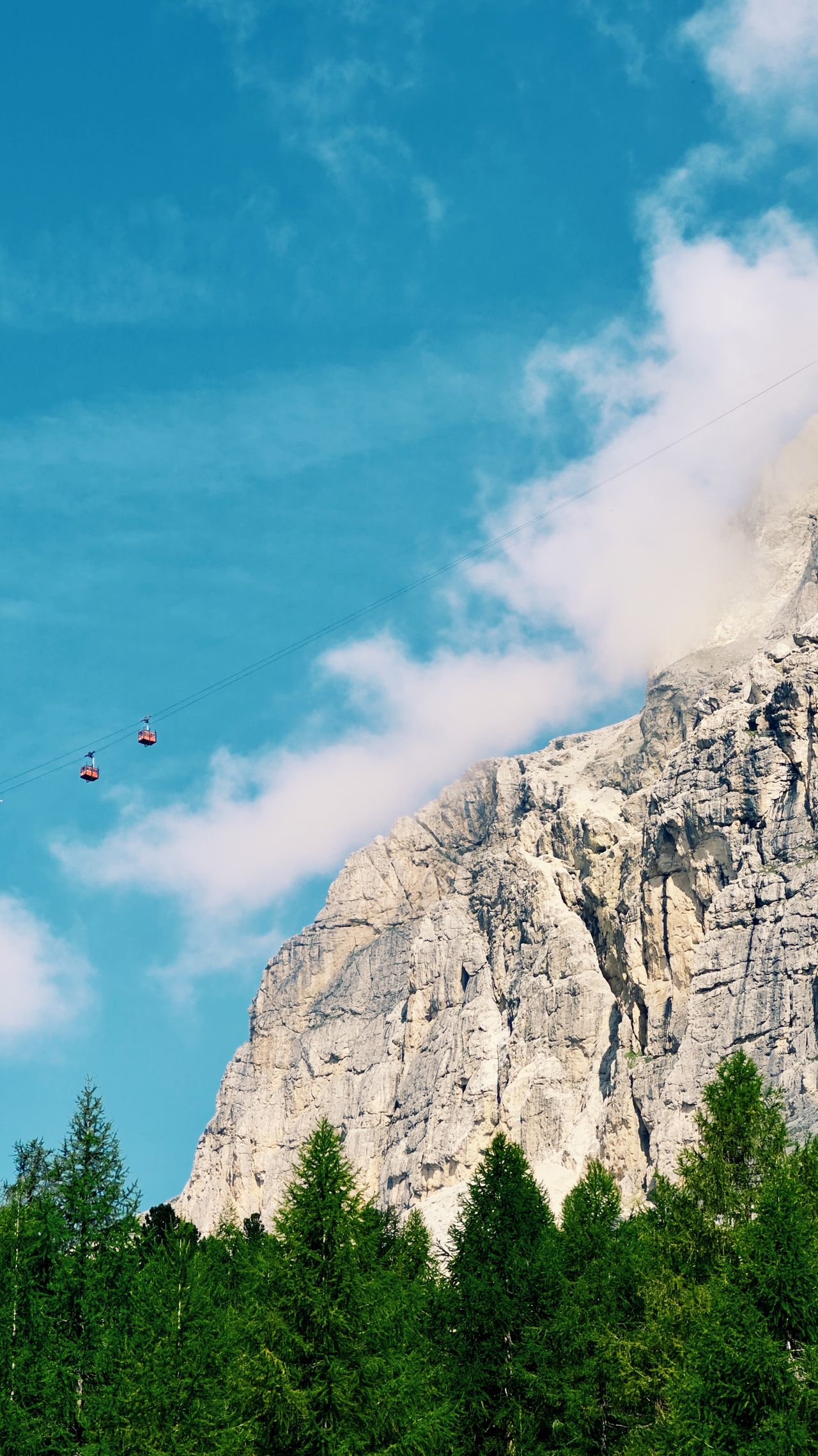 Cable car gondola rising above alpine forest towards rocky Dolomite peaks near Cortina d'Ampezzo, Italy