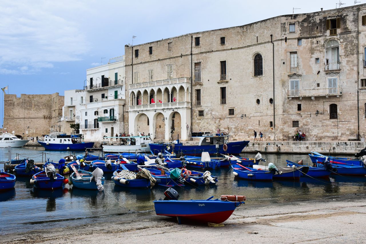 Colourful fishing boats moored in Monopoli harbour with stone buildings and church bell tower behind, Apulia, Italy