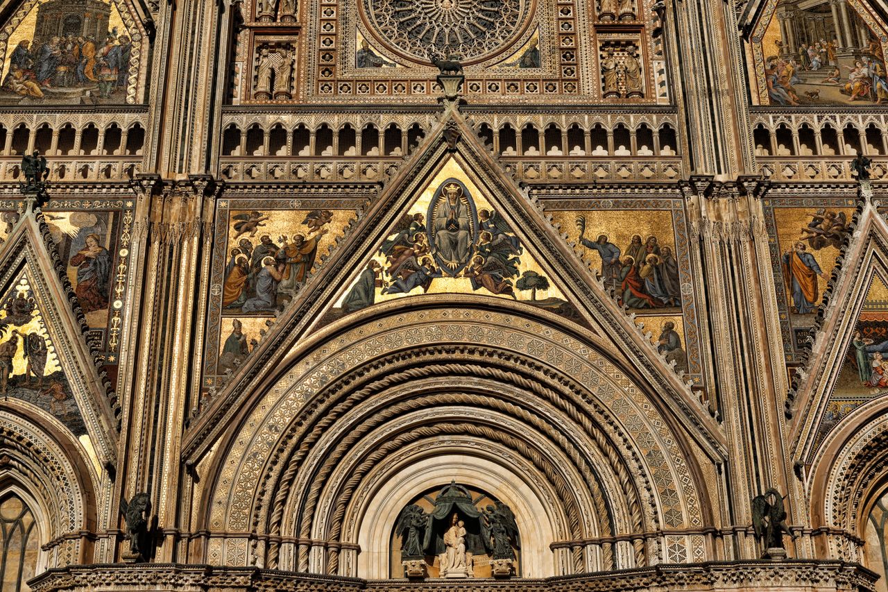 Ornate Gothic mosaic facade of Orvieto Cathedral against blue sky, Umbria, Italy