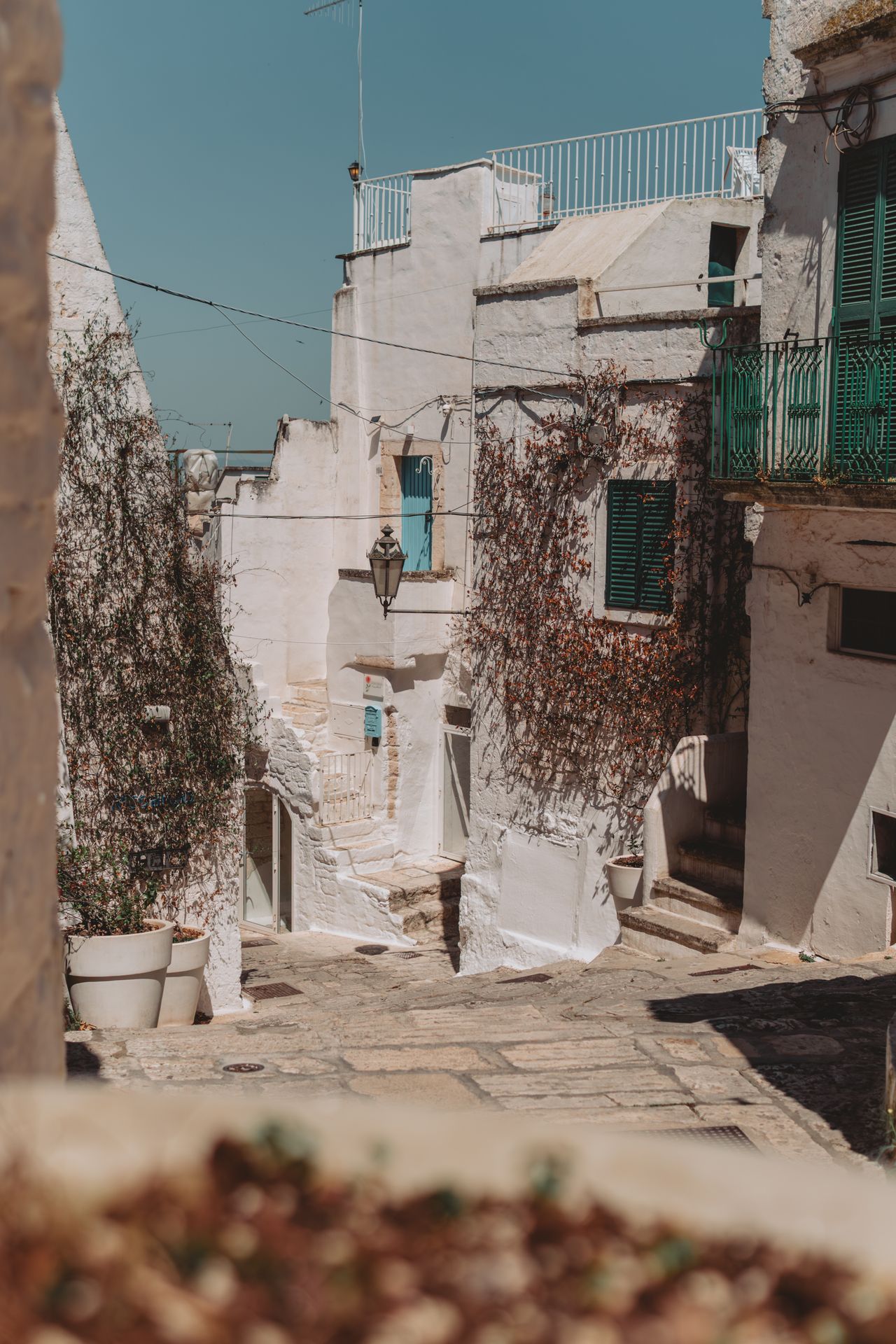 Narrow sun-drenched whitewashed alleyway in Ostuni old town with plant pots on steps, Apulia, Italy