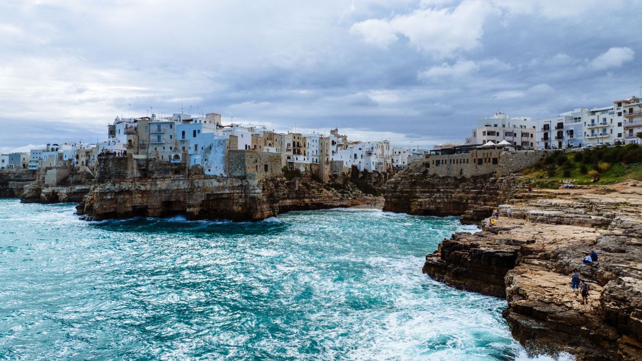 Historic white buildings perched dramatically on limestone cliffs above the clear blue Adriatic Sea in Polignano a Mare, Puglia, Italy