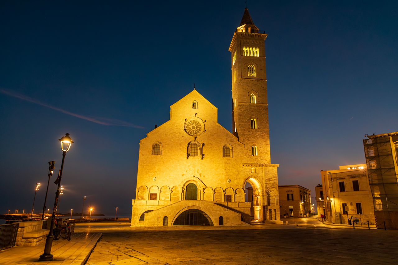 Trani Cathedral lit in golden light at dusk beside the Adriatic Sea with its Romanesque bell tower, Puglia, Italy