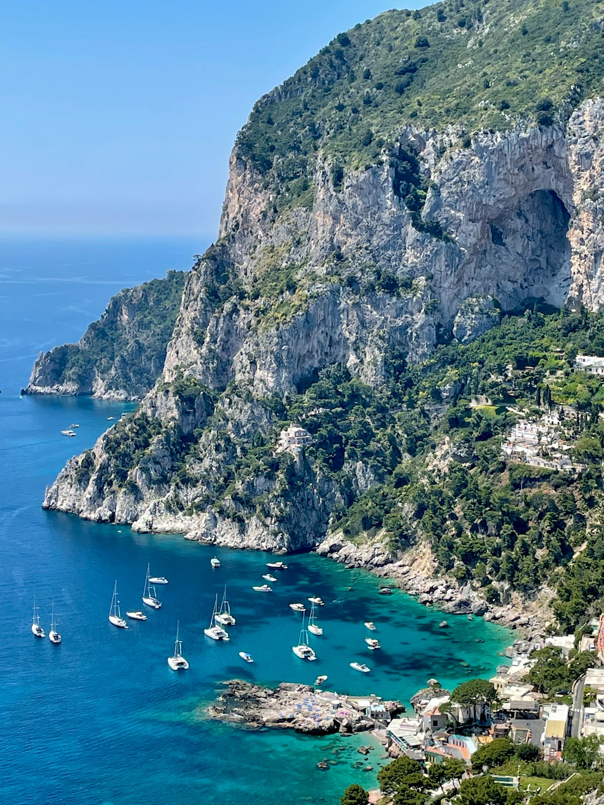 Sailing boats moored in turquoise water beneath dramatic limestone cliffs, Capri, Italy