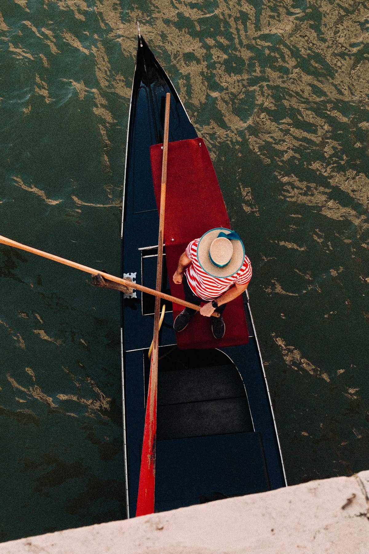 Gondolier in straw hat rowing a gondola on a Venice canal, seen from above