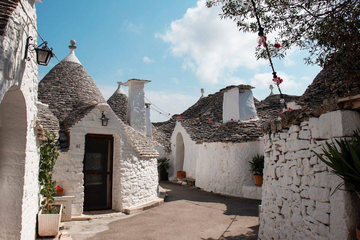 Whitewashed trulli houses with conical stone roofs on a sunny street in Alberobello, Puglia, Italy