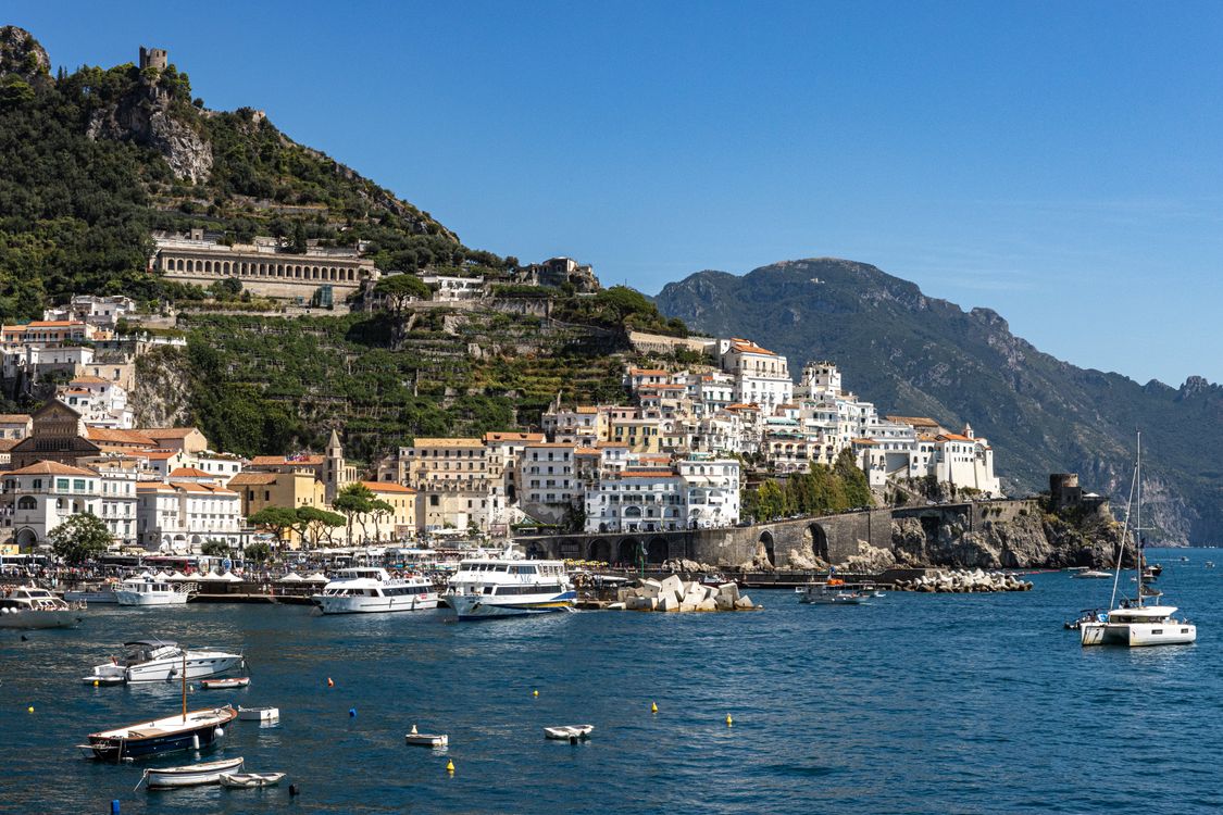Amalfi town from the sea with boats in the harbour and buildings climbing the hillside, Italy