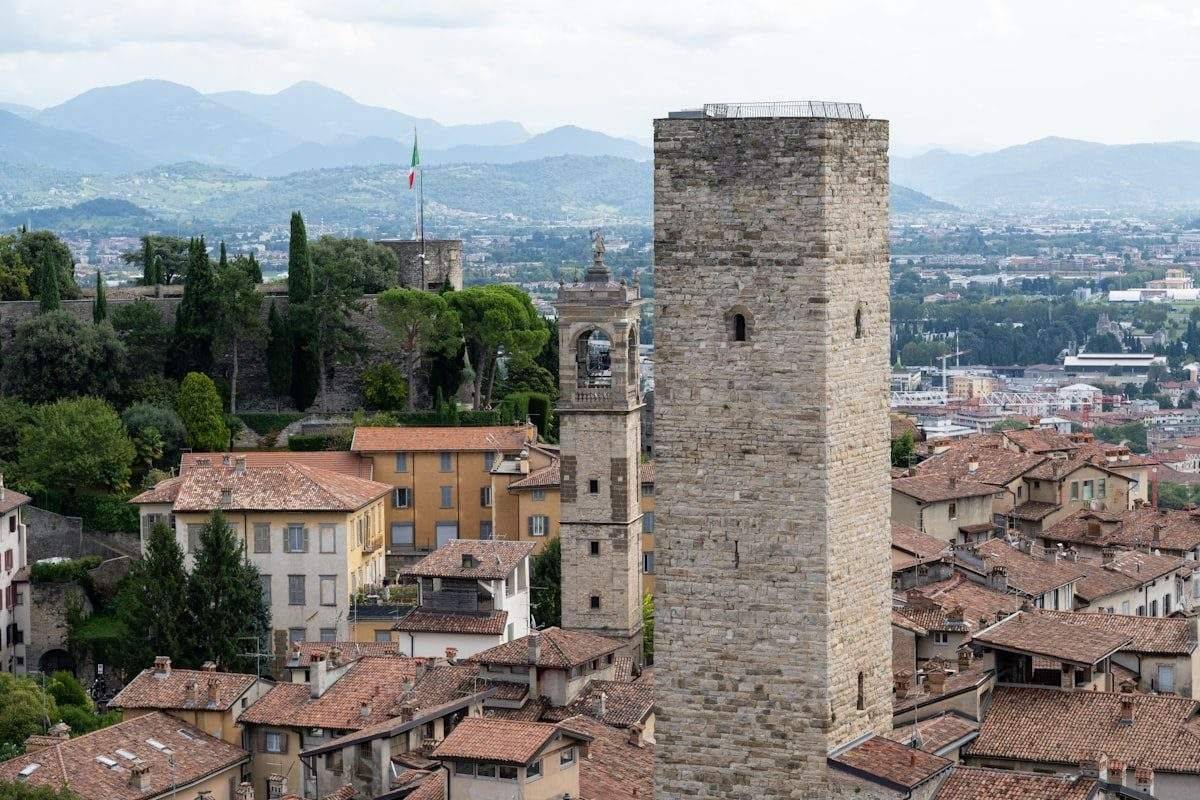 The stone tower and rooftops of Bergamo Alta with alpine foothills behind, Lombardy, Italy
