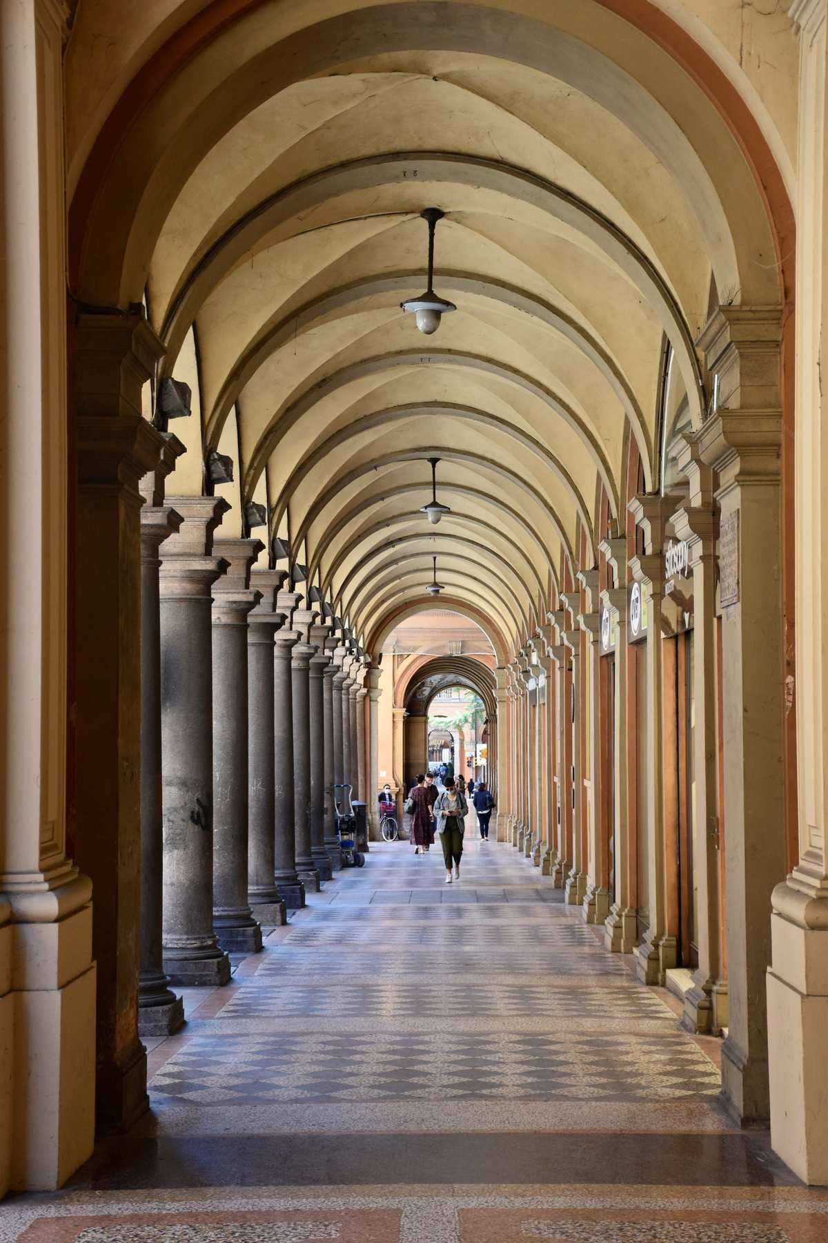People walking through a historic arched portico arcade, Bologna, Emilia-Romagna, Italy