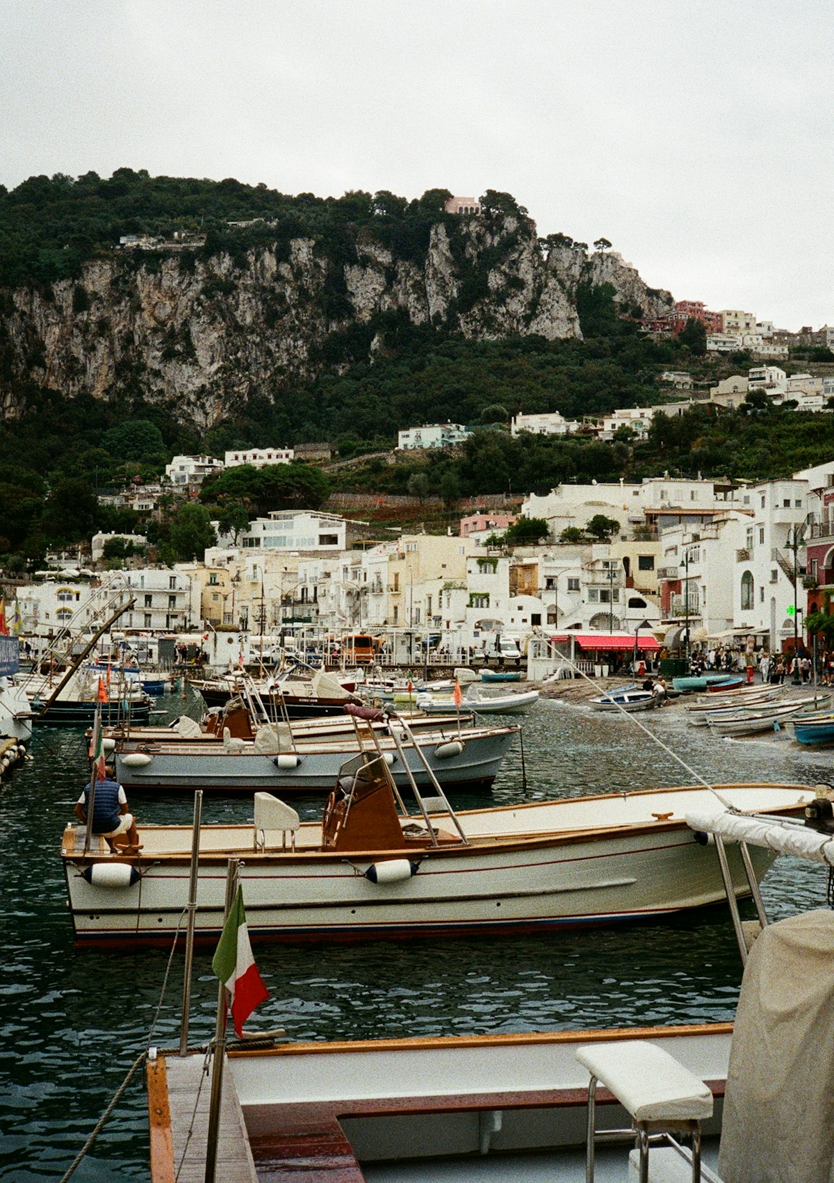 Wooden boats moored at Marina Grande harbour with white buildings and rocky cliffs behind, Capri, Bay of Naples