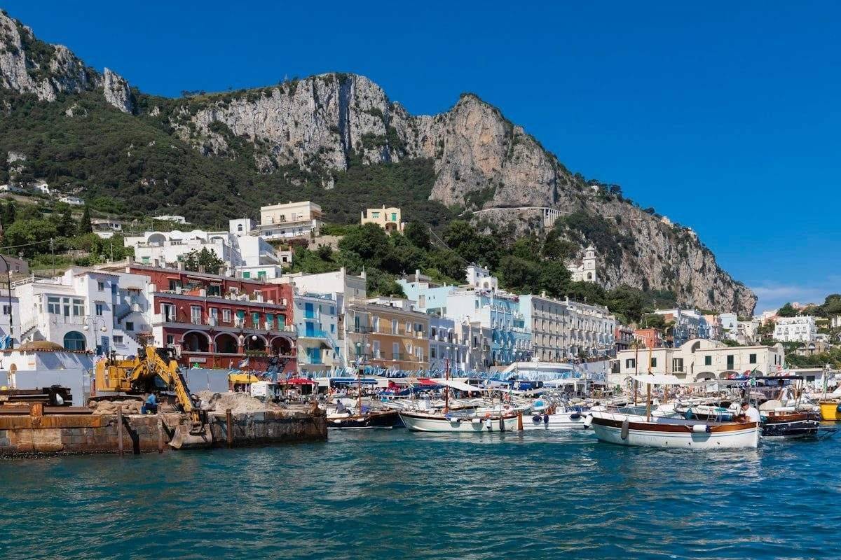 Colourful waterfront buildings at Capri marina with boats and rocky mountains, Bay of Naples, Italy