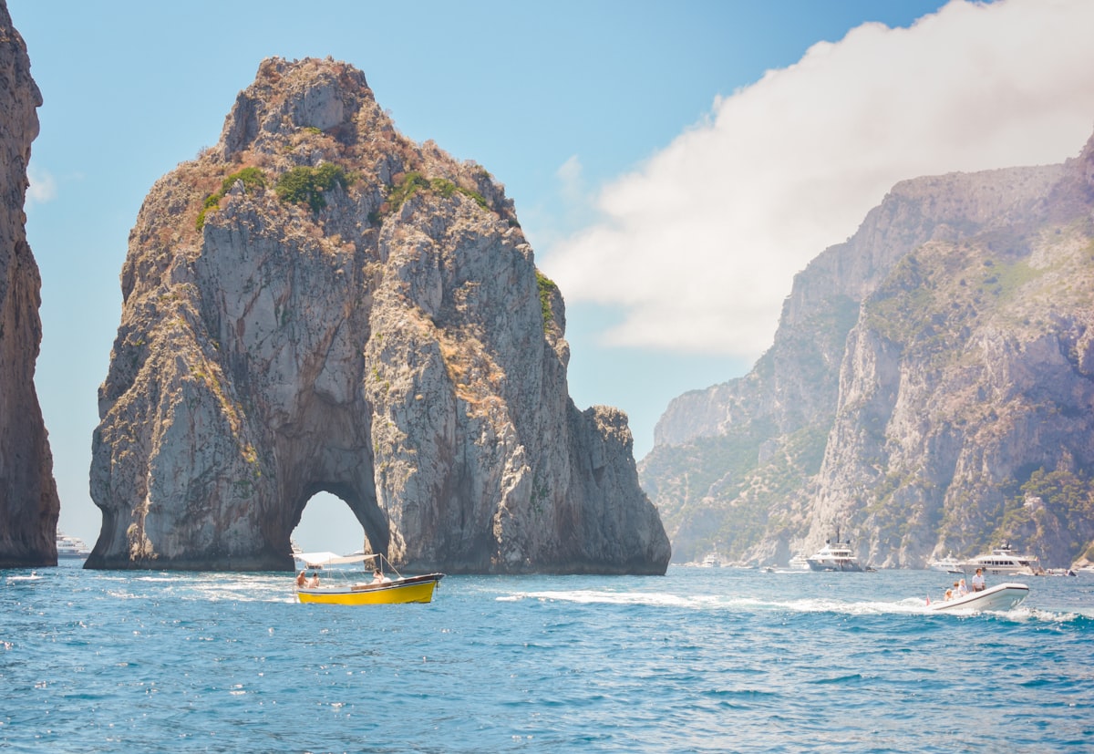 Boats sailing past the famous Faraglioni rock arches, Capri island, Bay of Naples, Italy