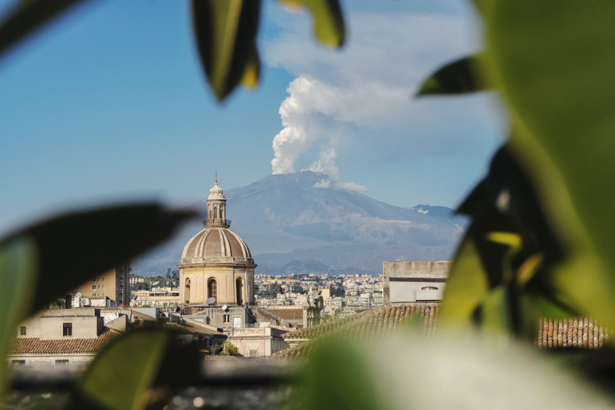 Catania city rooftops with Mount Etna emitting smoke in the background