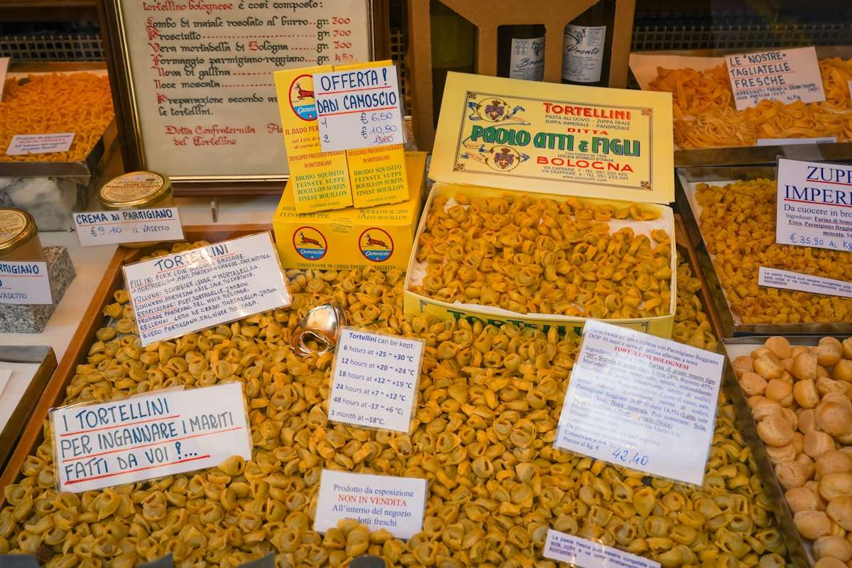 Various dried pasta shapes — fusilli, rigatoni, farfalle — displayed at an Italian market stall