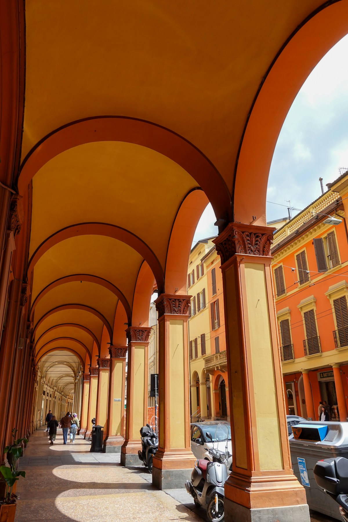 Historic orange and yellow portico with people walking, Bologna, Italy