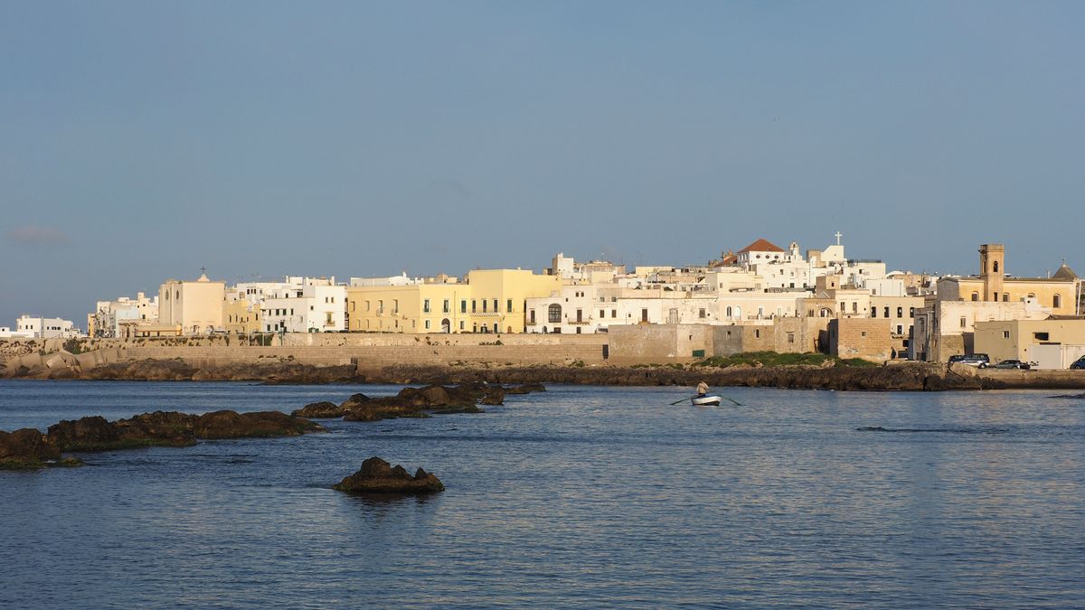 Gallipoli island old town viewed from across the Ionian Sea, with white and yellow buildings along the sea walls, Puglia, Italy