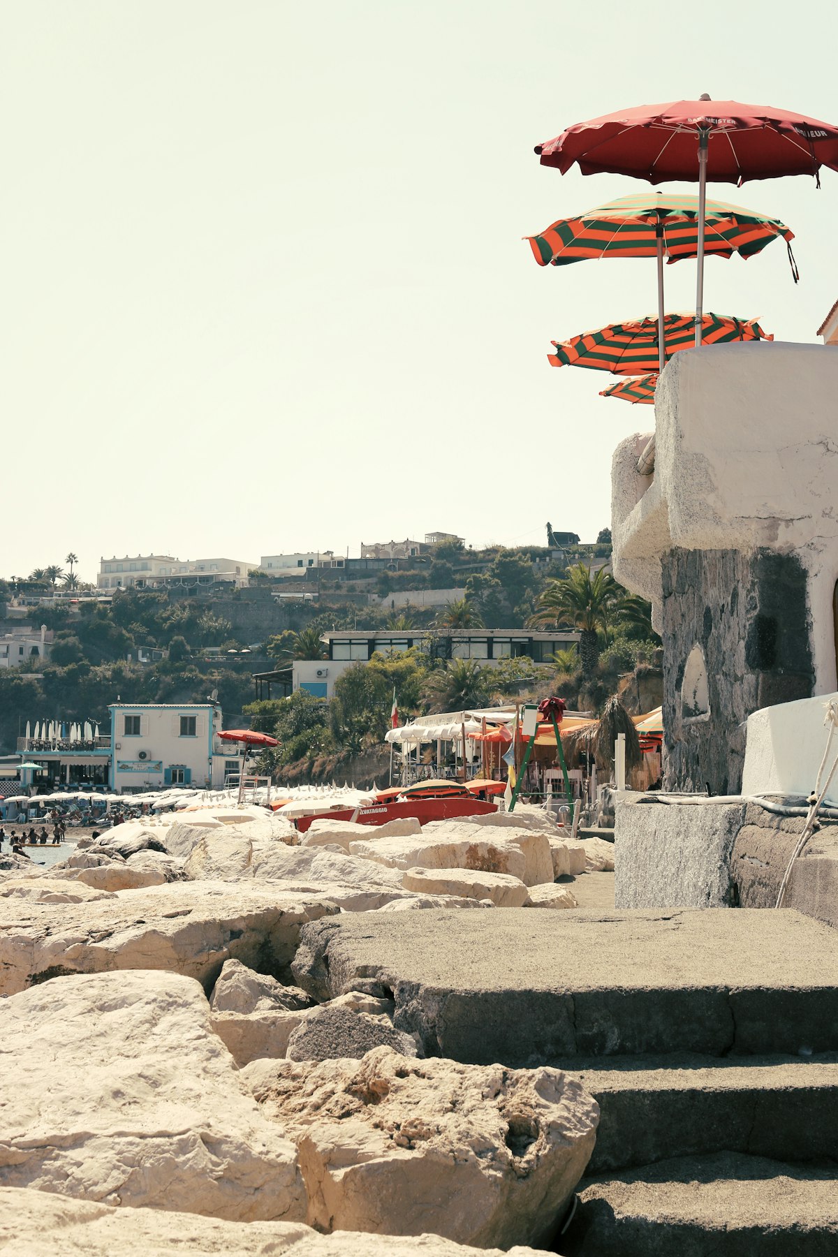 Beach umbrellas and sun loungers at a rocky bay, Ischia, Bay of Naples, Italy