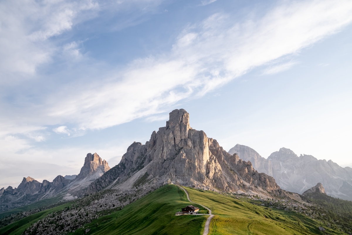 Dramatic rocky Dolomite peaks at Passo Giau above alpine meadows with a chalet, Belluno province, Italy