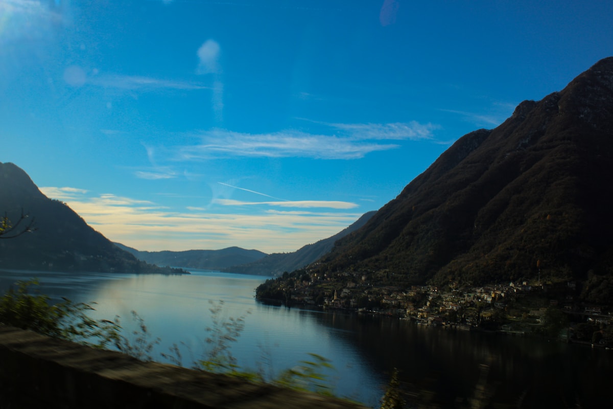 An Italian lake between steep forested mountains at dusk with a village on the shoreline, northern Italy
