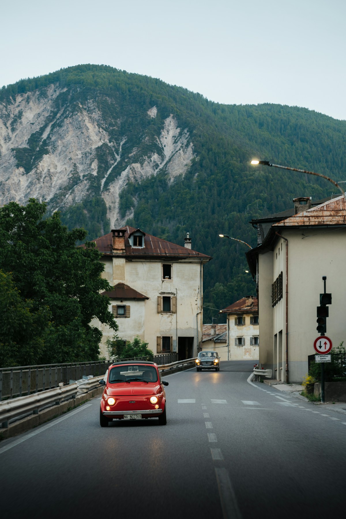 Classic red Fiat 500 driving on a mountain road through an Italian village