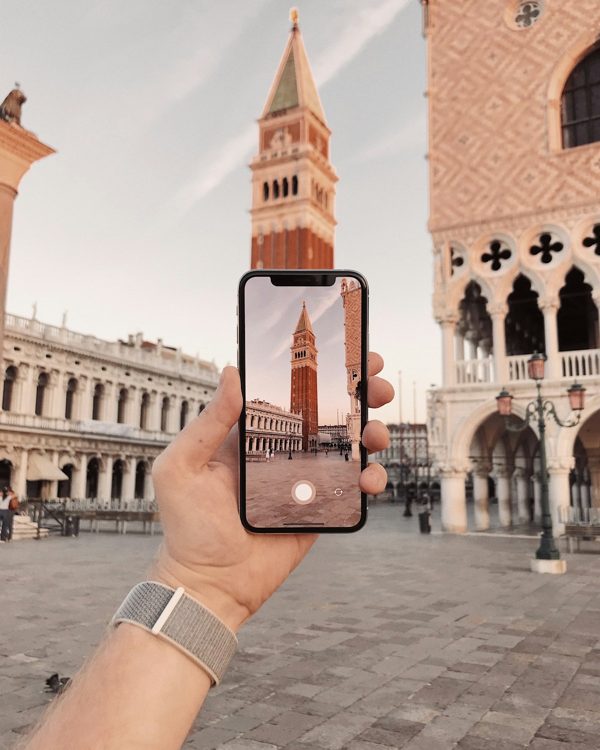 Person taking a picture of a clock tower in Venice, Italy — travel costs