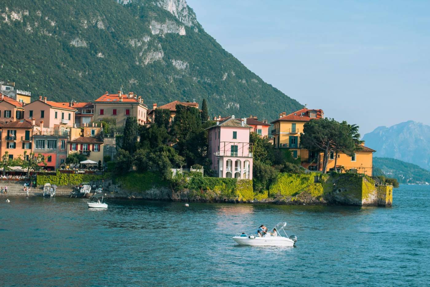 Group of people in a boat approaching Varenna village on Lake Como with Alpine peaks behind, Italy