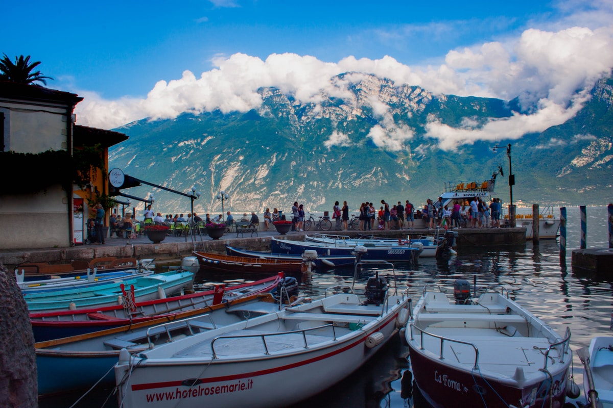 Small boats moored in a Lake Garda harbour with mountains behind, northern Italy