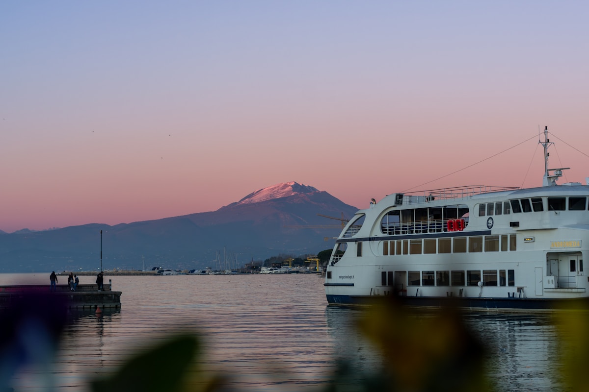 Ferry boat docked at Lake Garda at sunset with snow-capped mountain behind, northern Italy