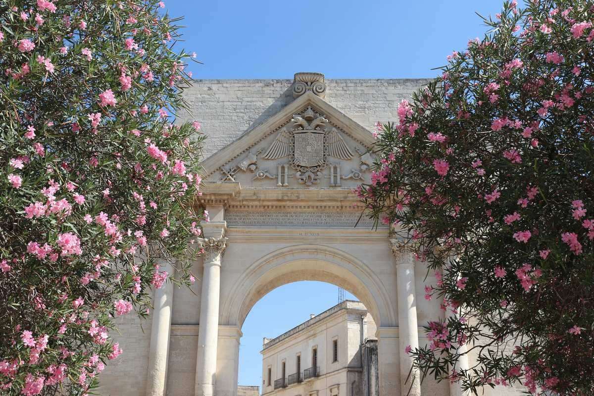 Ancient stone archway framed by pink oleander flowers in the baroque old town of Lecce, Puglia, Italy