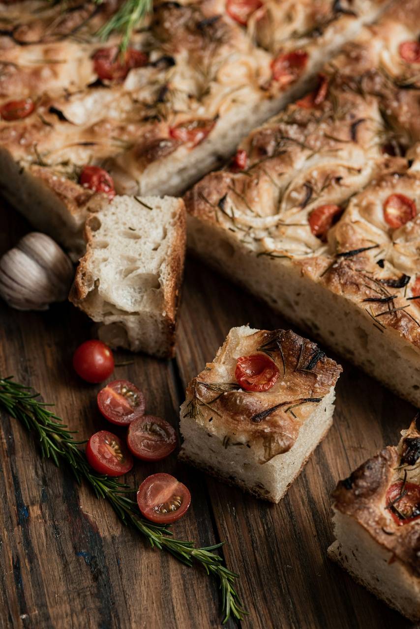 Focaccia bread topped with cherry tomatoes and rosemary on a wooden board, Italian baked goods