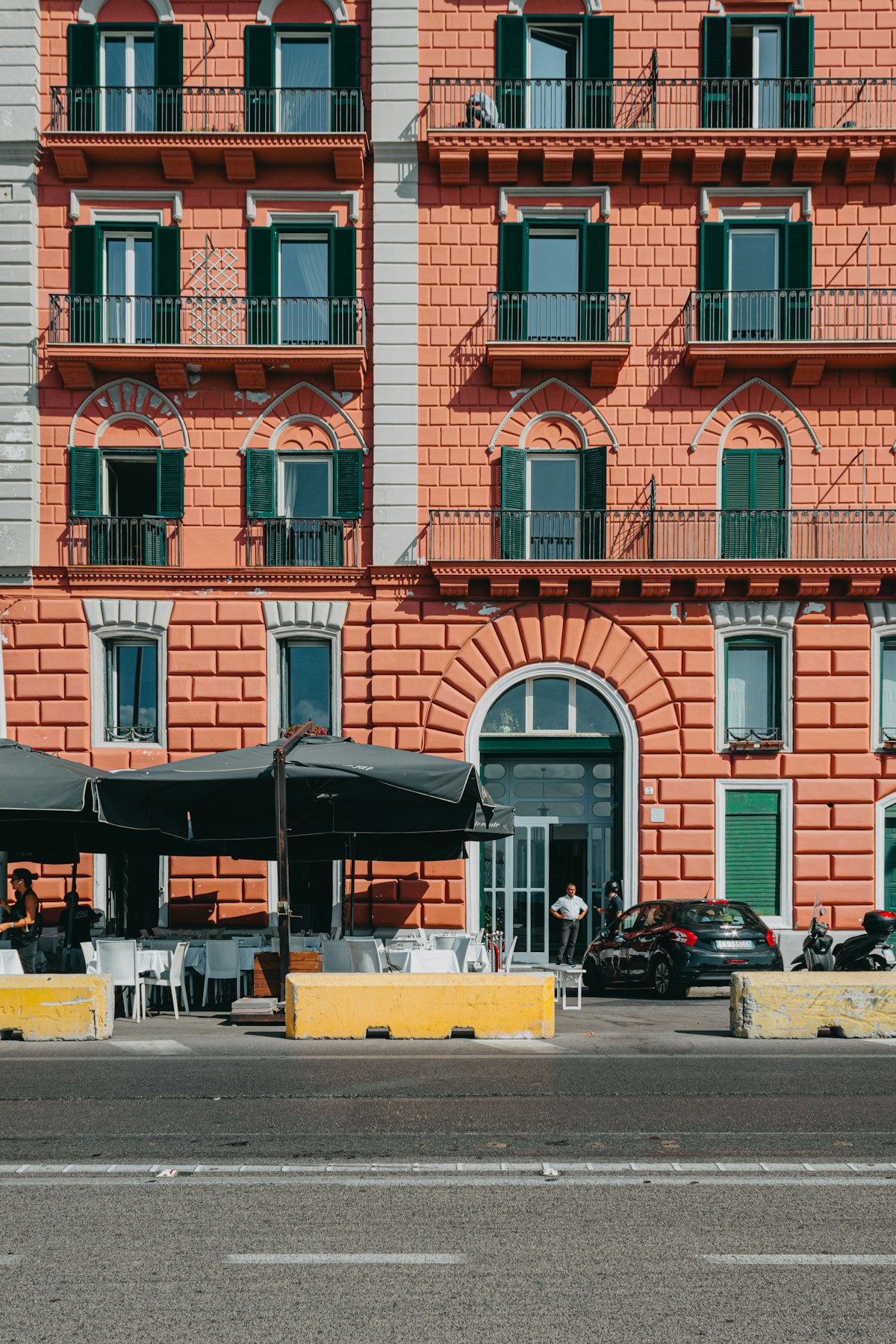 Coral-red building facade with green shutters and outdoor cafe tables, Naples, Campania, Italy