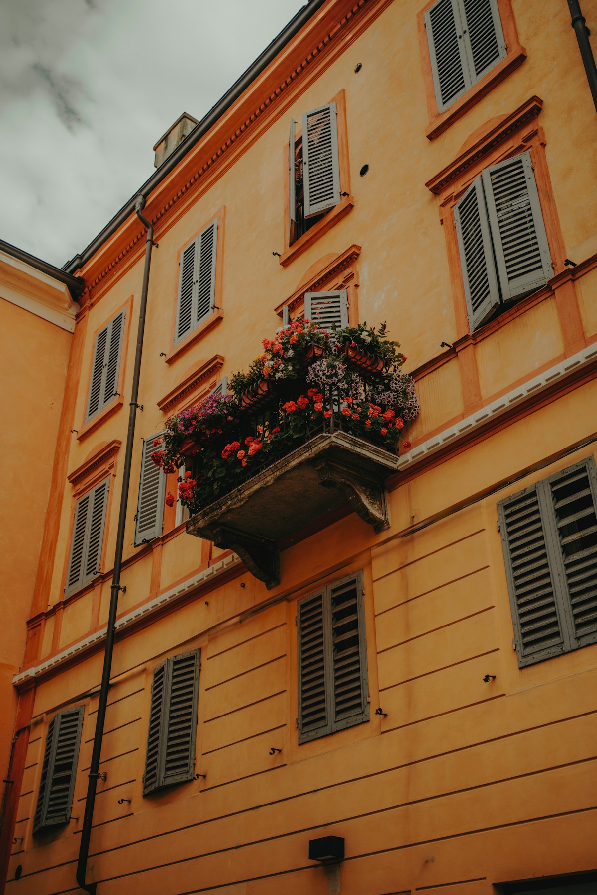Orange building with flower-filled balcony on a sunny street in Parma, Emilia-Romagna, Italy