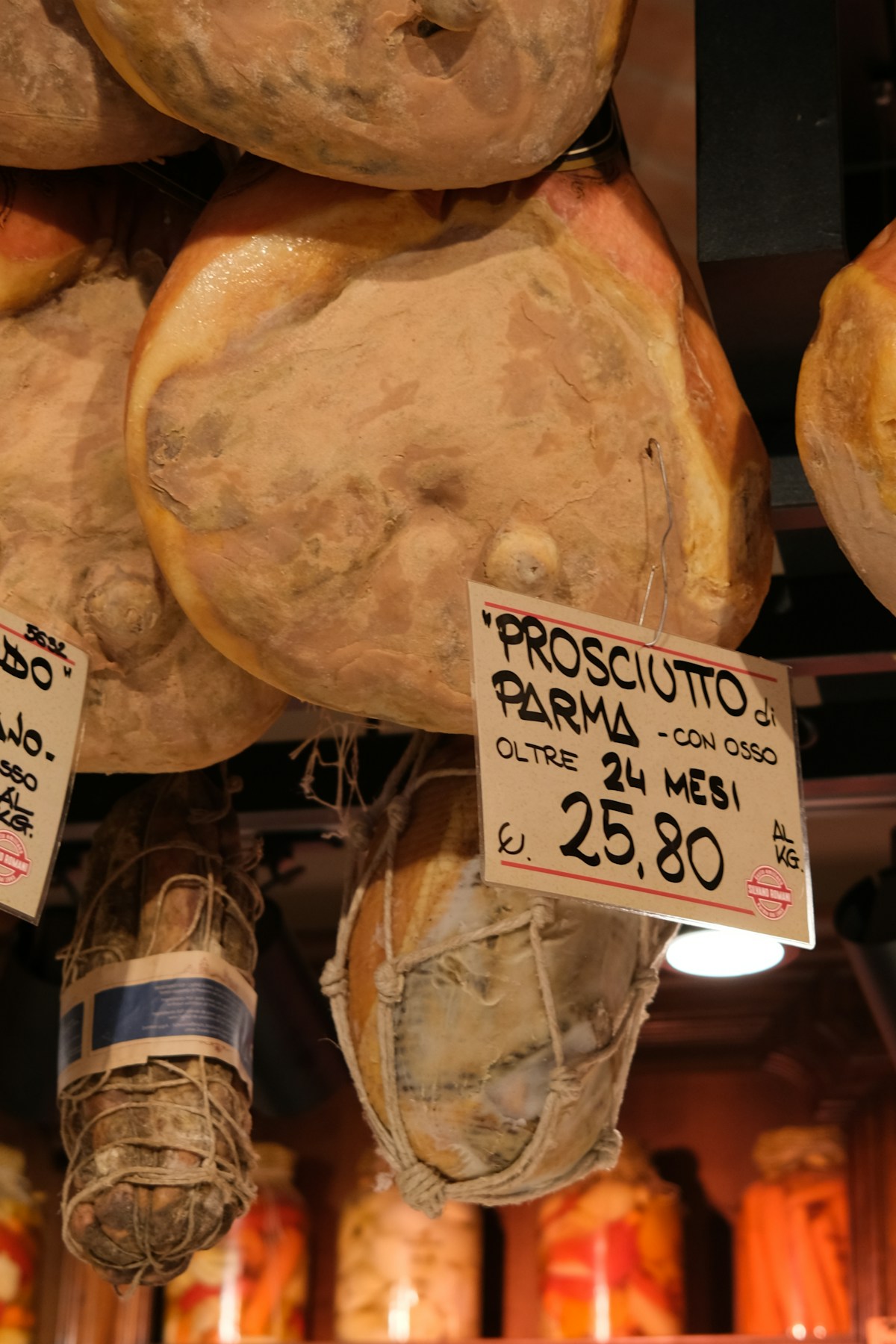 Prosciutto di Parma legs hanging in a curing market with price tag, Parma, Emilia-Romagna, Italy