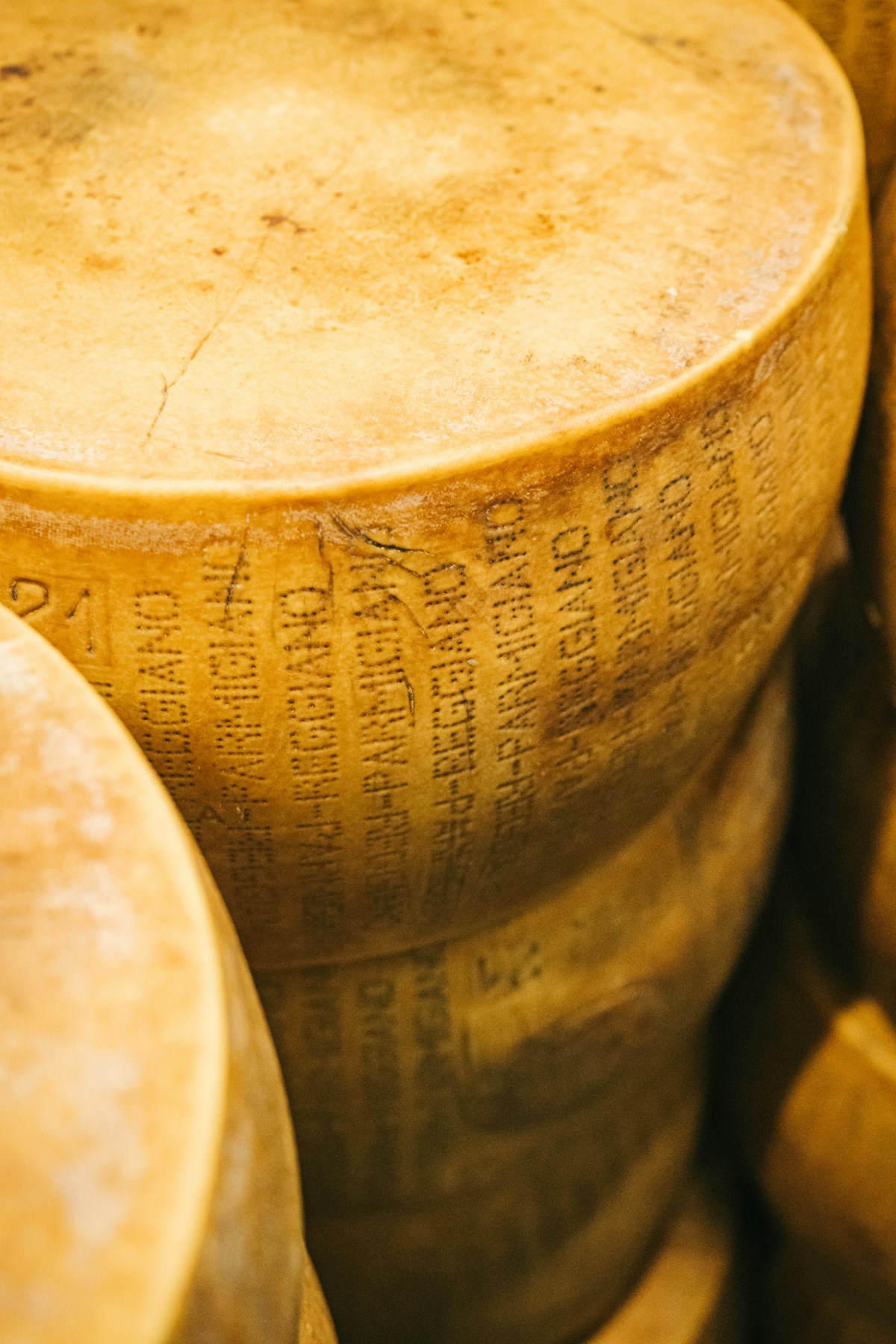 Aged Parmigiano Reggiano wheels stacked on shelves with branding stamp visible, Emilia-Romagna, Italy