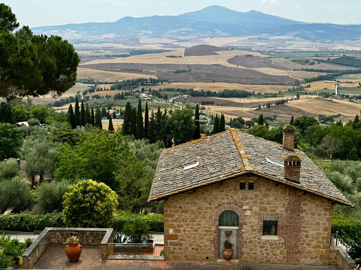 The Renaissance façade of the Duomo rising above the small piazza of Pienza, with the Val d'Orcia landscape visible beyond