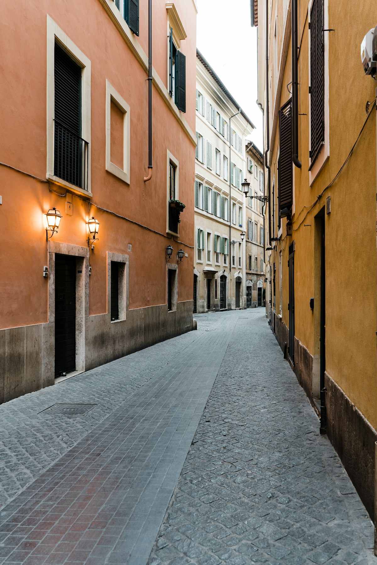 Cobblestone alley with warm ochre buildings and lanterns in central Rome, Italy