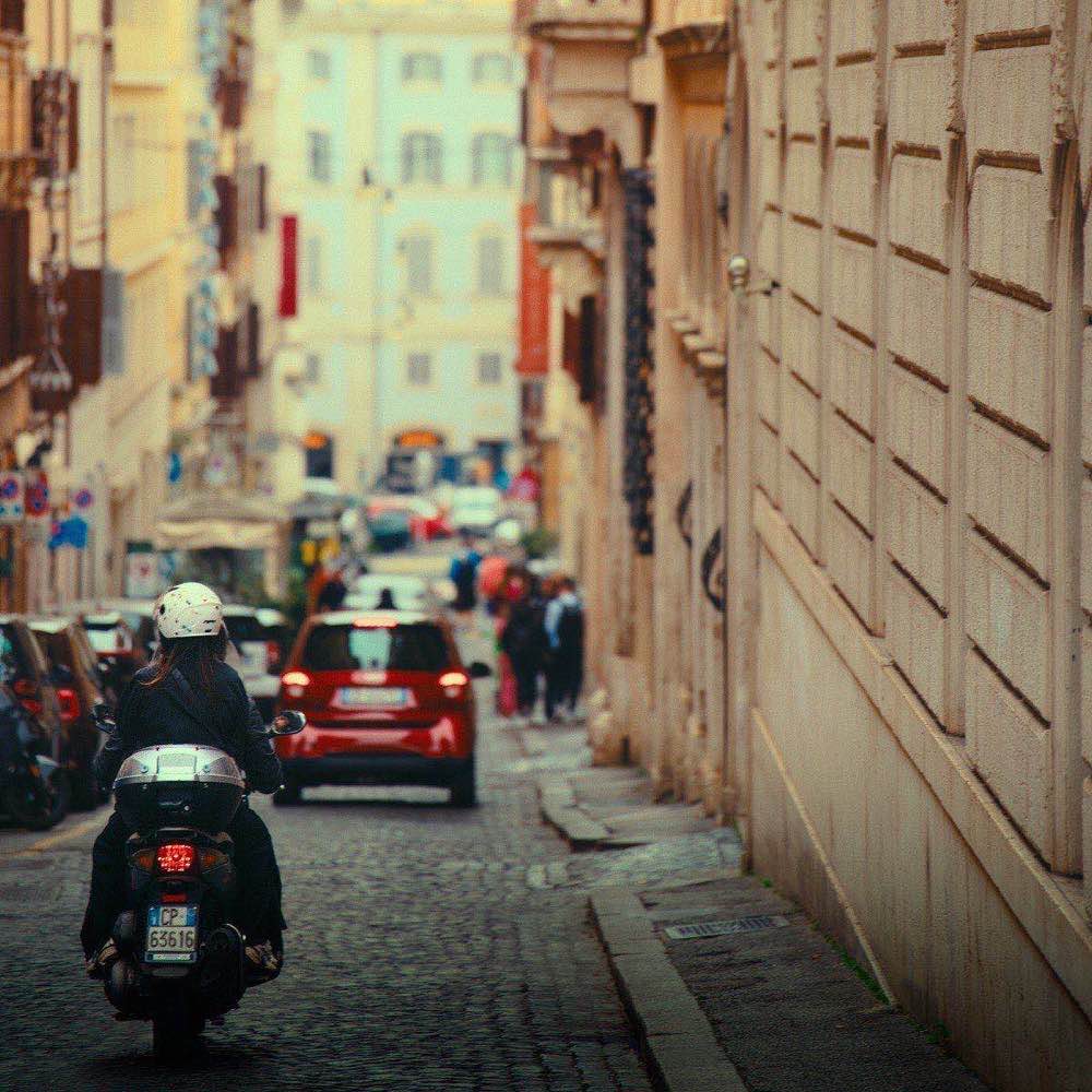 Vespa scooter navigating a cobblestone street past terracotta buildings in a Rome residential neighbourhood