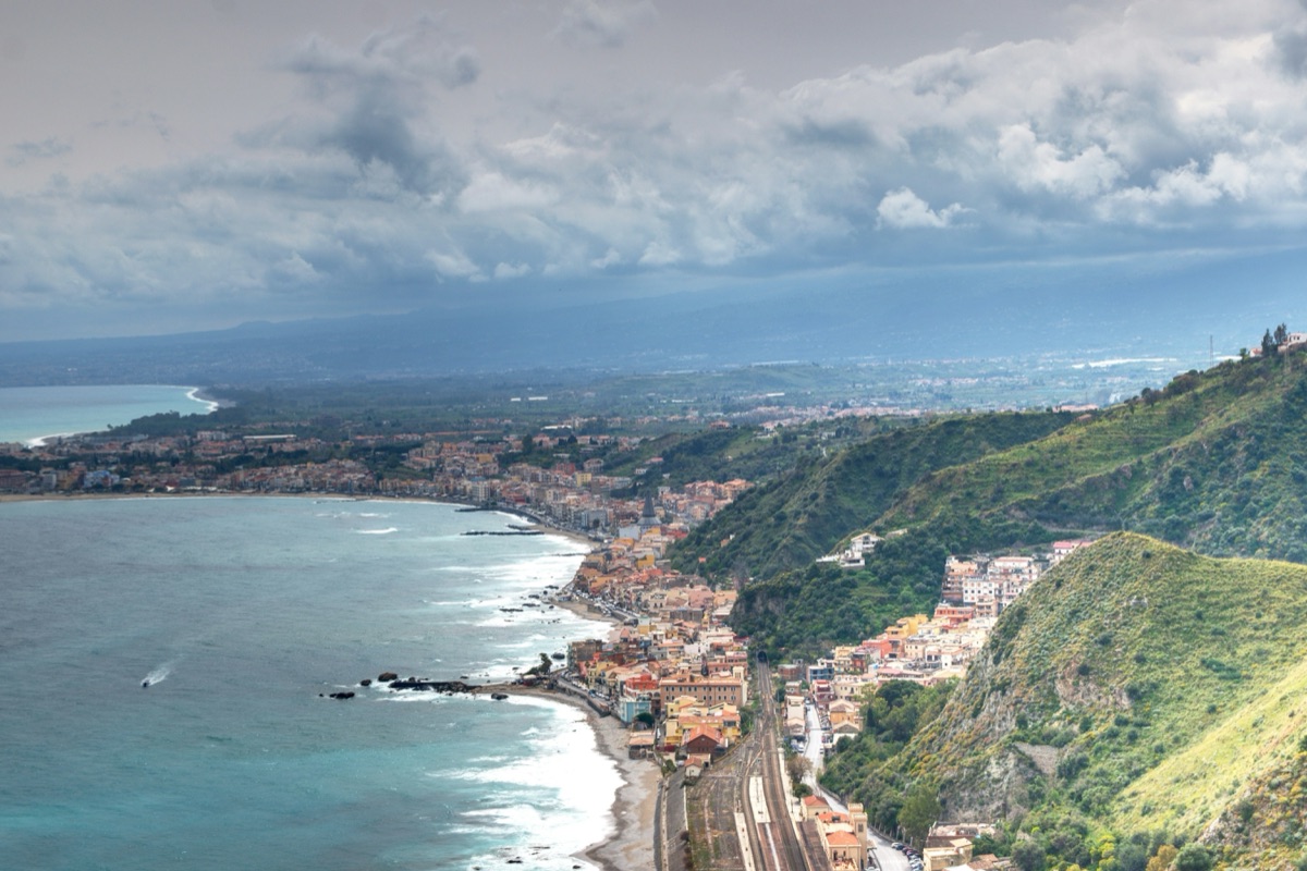 Aerial view of the Sicilian coastline south of Taormina with the turquoise Mediterranean sea and villages climbing the hillside