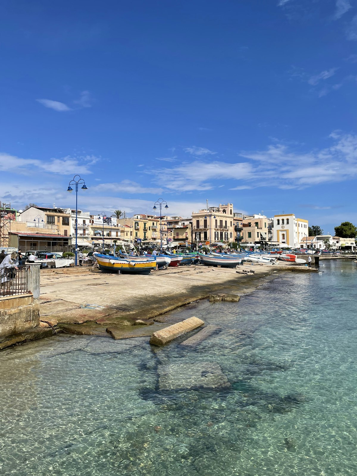 Colourful fishing boats moored at a Sicilian harbour with clear turquoise water and golden buildings lining the waterfront