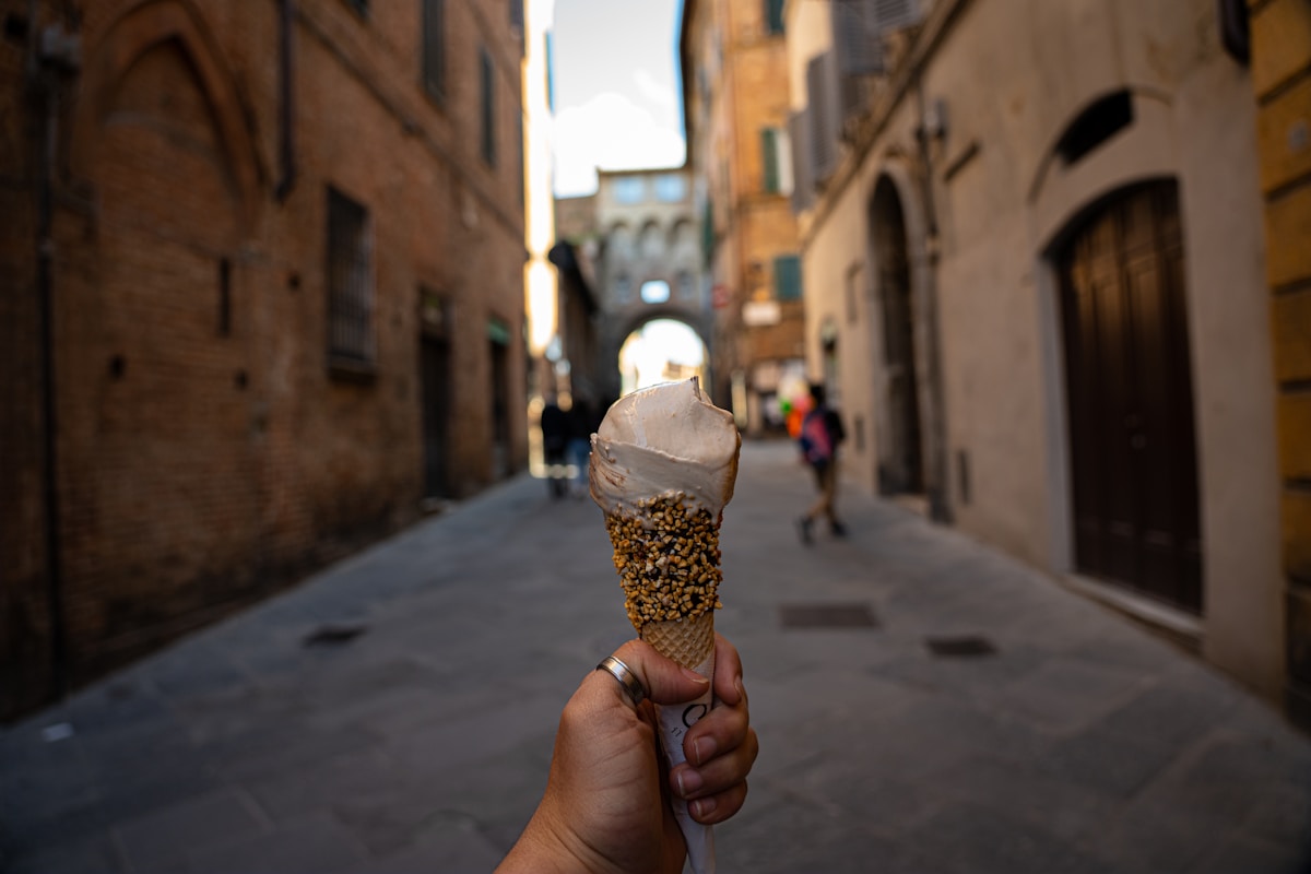 Gelato cone held up on a narrow medieval street in Siena, Tuscany, Italy