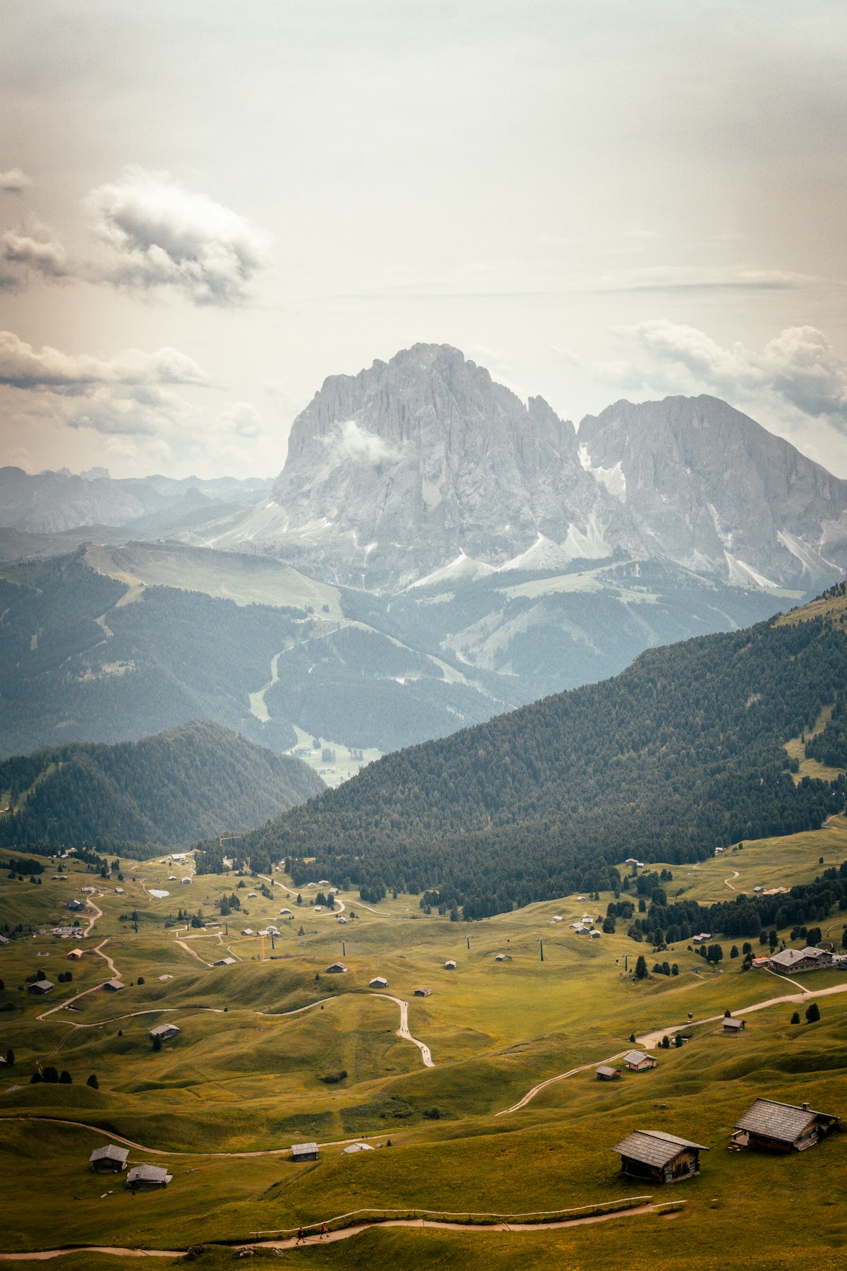 Green alpine valley with scattered mountain huts and a dramatic rocky Dolomites peak, Trentino, Italy