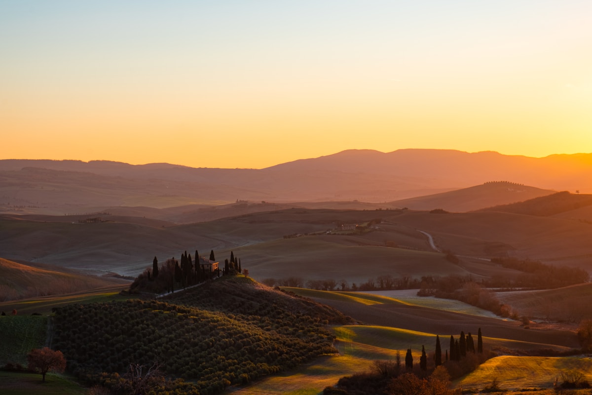 Rolling Tuscan hills with cypress trees and a farmhouse at golden hour sunset, Val d'Orcia, Italy