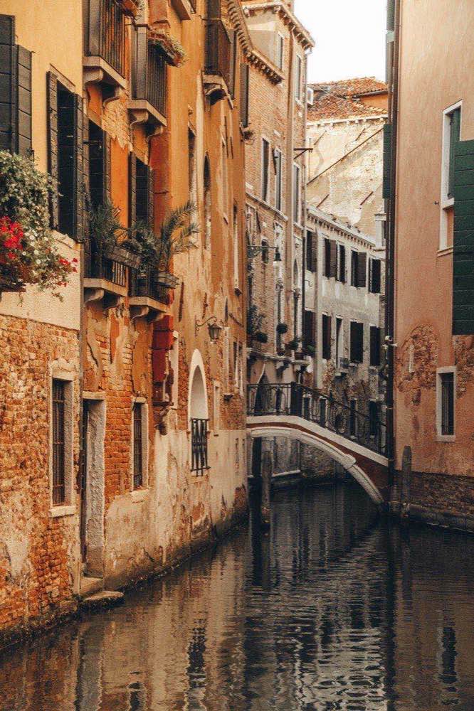 Narrow residential canal with old terracotta buildings and a small stone bridge in Venice