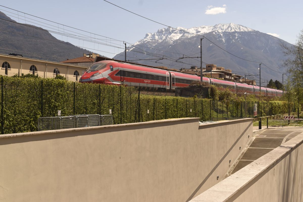 Red Frecciarossa high-speed train passing through alpine northern Italy with snow-capped mountains