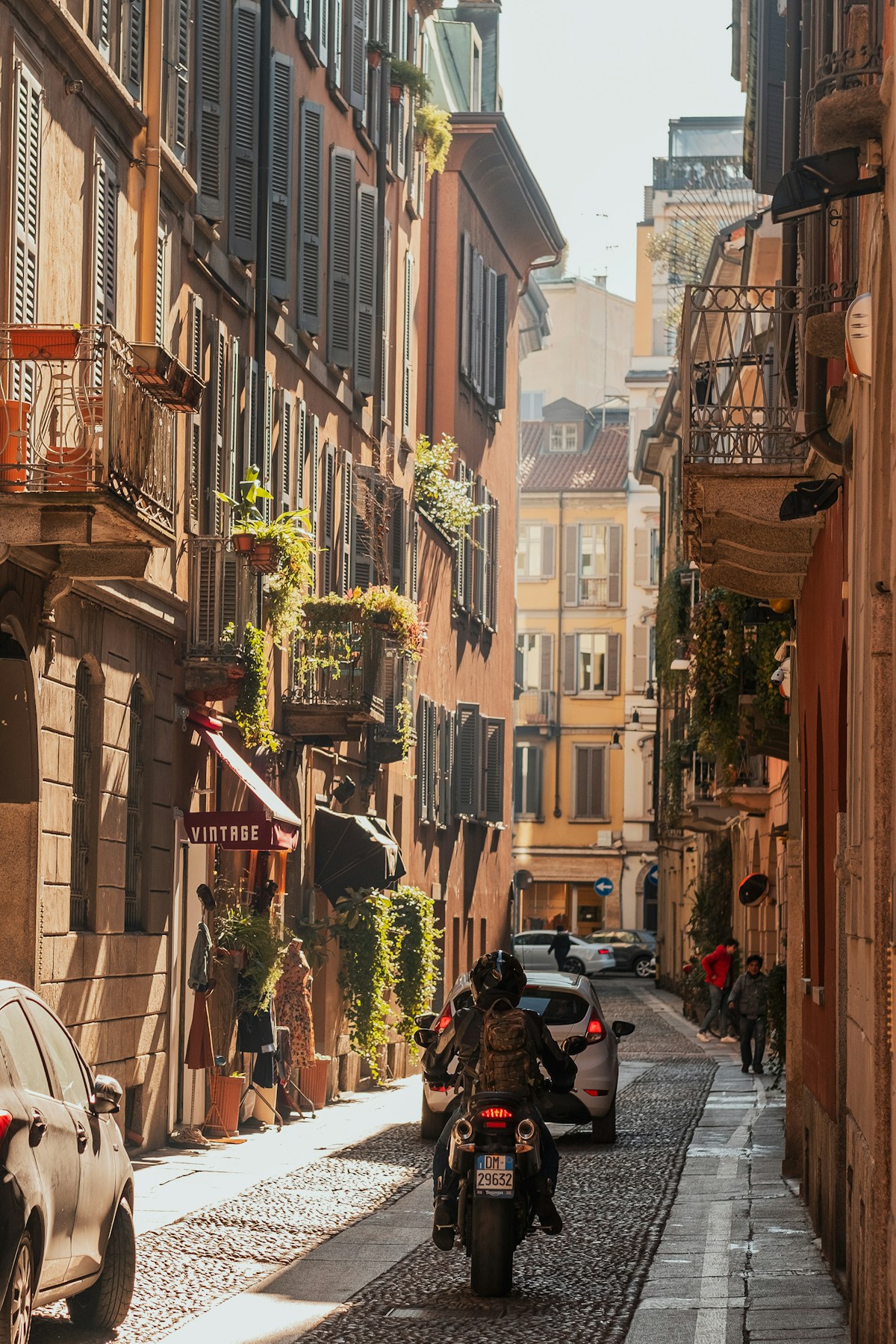 Narrow cobblestone street with traditional Milan buildings and a parked scooter, Lombardy, Italy