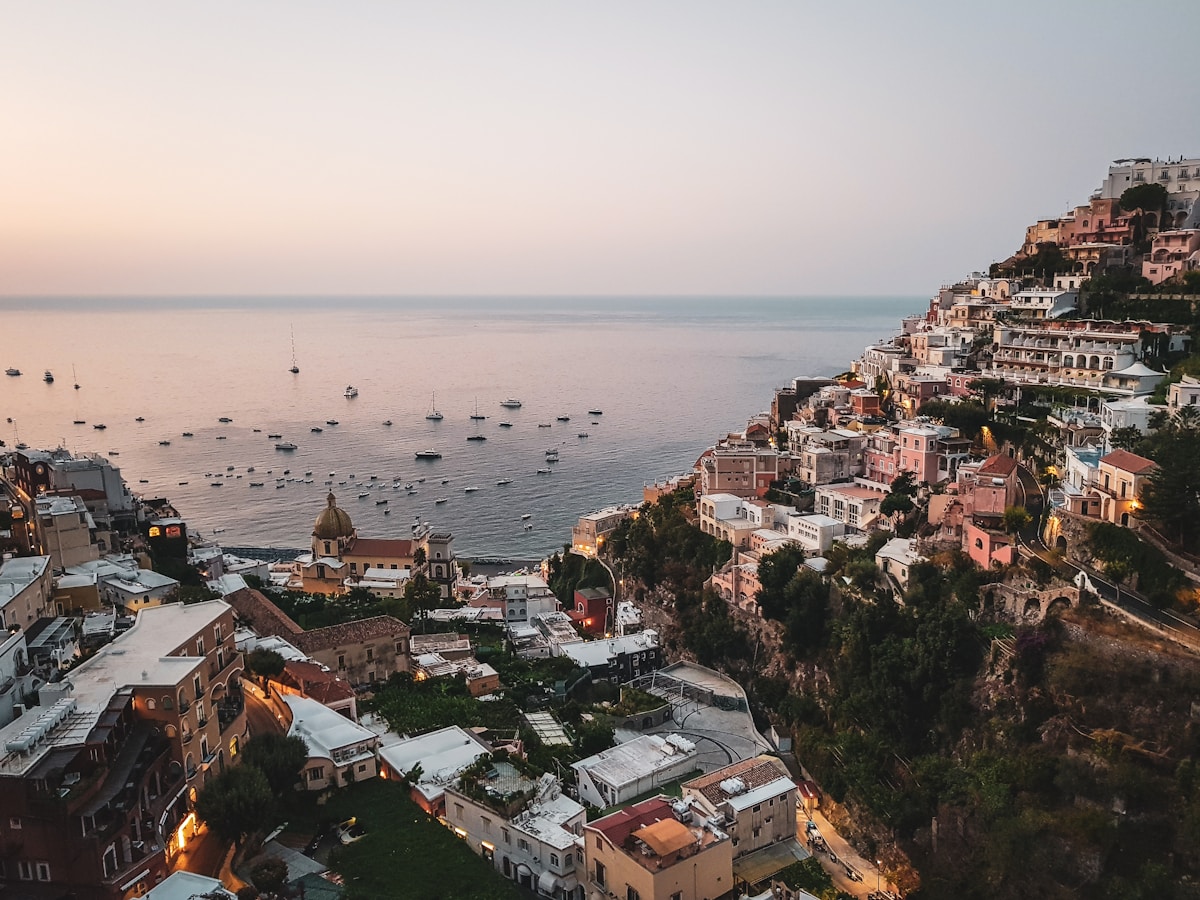 Positano hillside at dusk with tiered pastel buildings cascading down to the Amalfi Coast sea, Italy