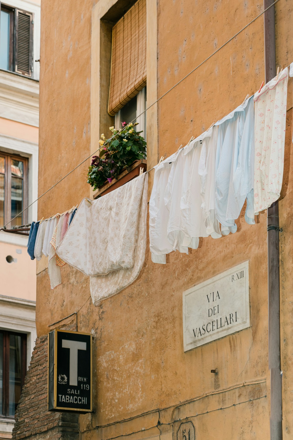 Trastevere street scene in Rome with laundry hanging above a Via dei Vascellari sign on an ochre building