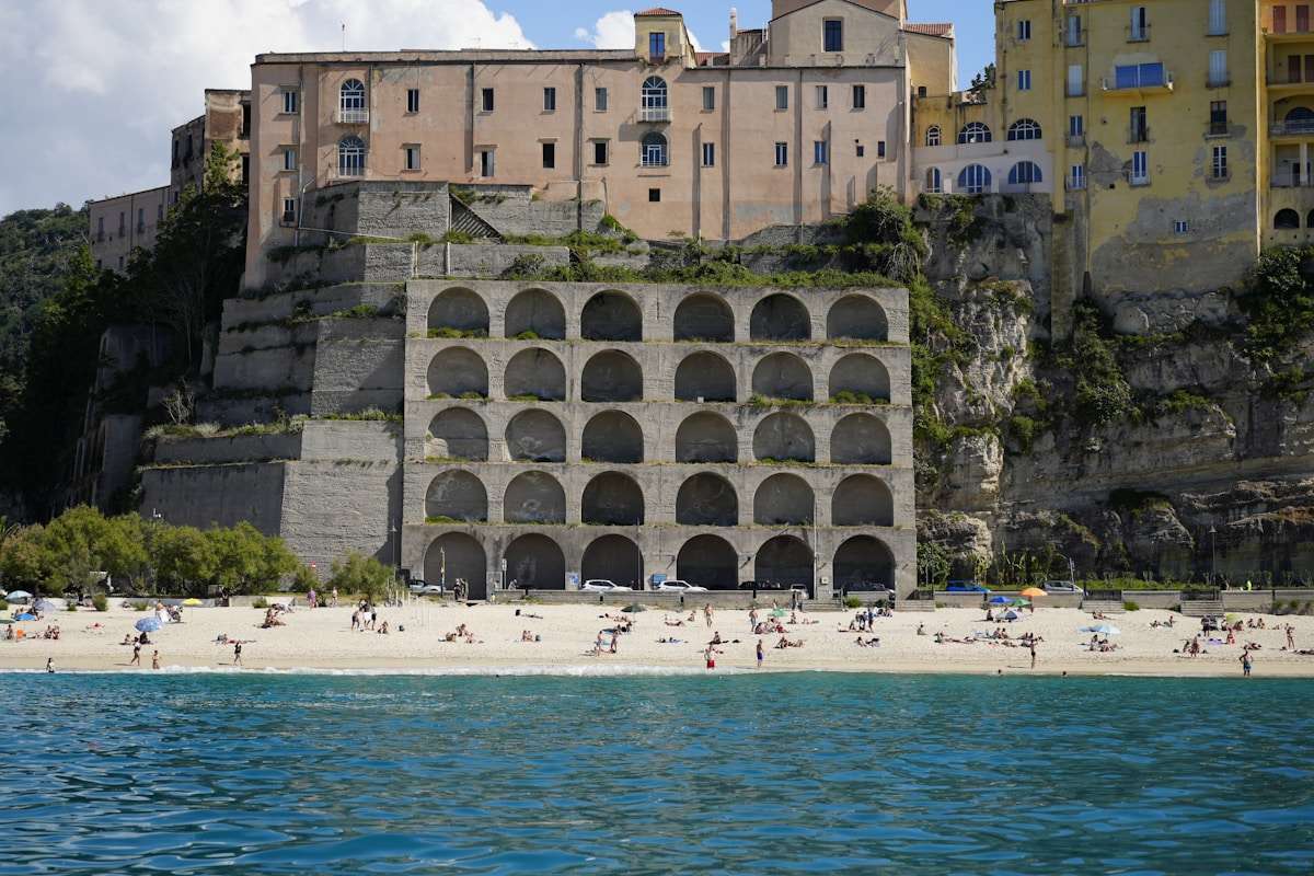 People relaxing on the white sand beach of Tropea below the clifftop town buildings, Calabria, Italy